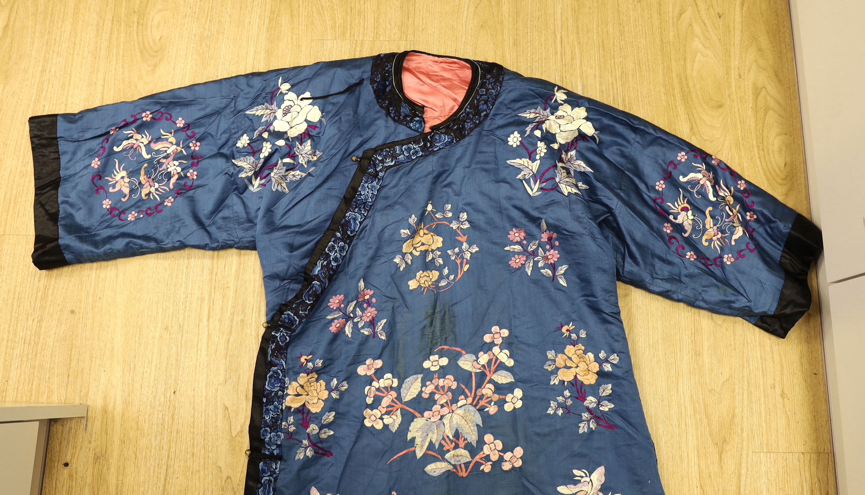 An early 20th century Chinese blue silk embroidered robe, later altered, cut and re-lined, together with various pieces of later Chinese embroidery and an earlier red silk panel with cut velvet circular motifs